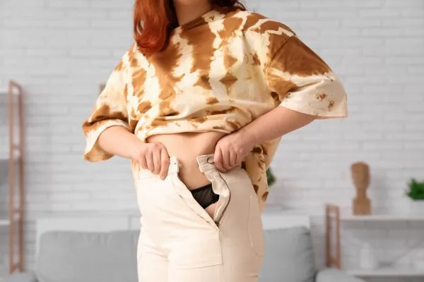 Image of woman trying to do her trousers up after pregnancy weight gain Northolt